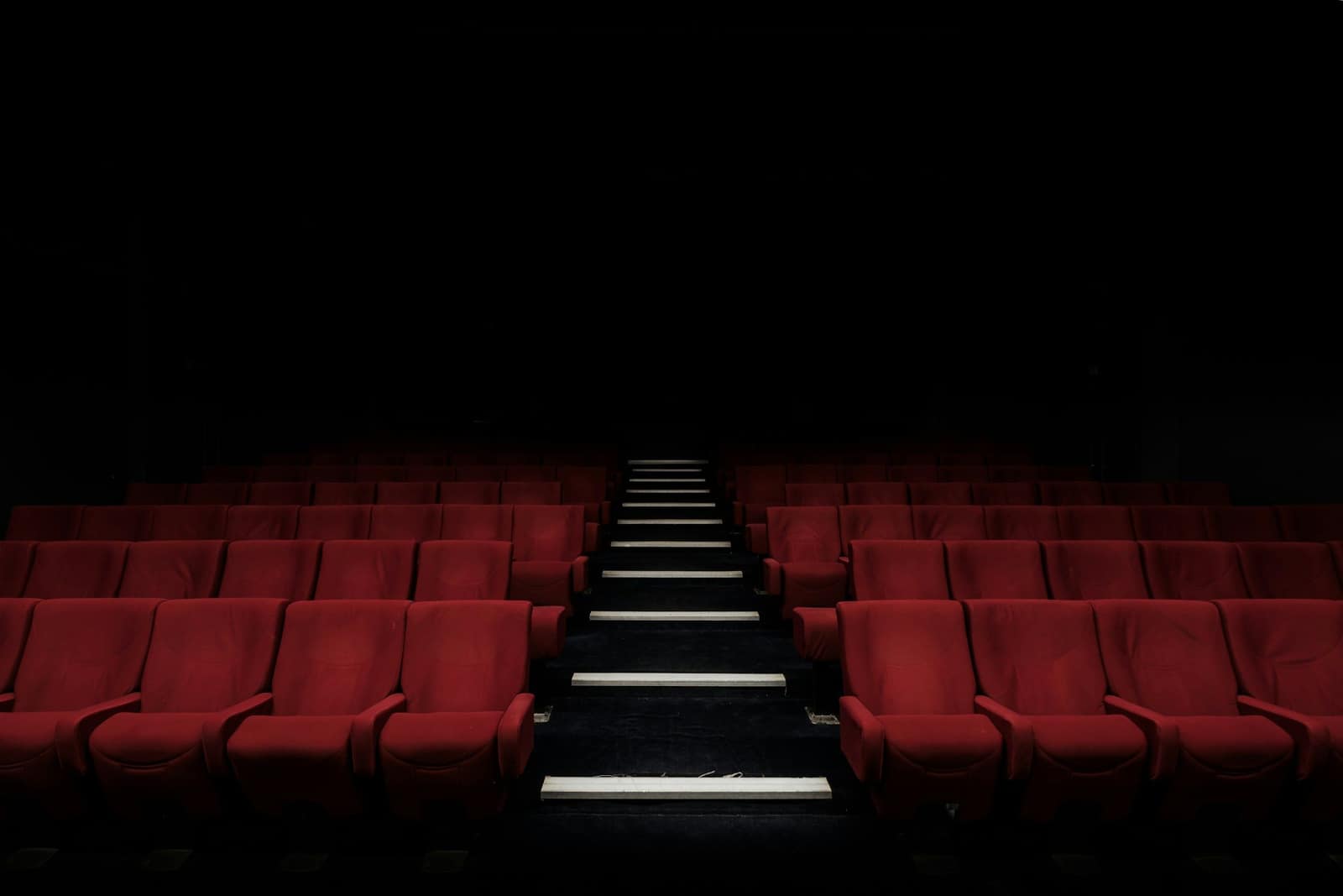 Rows of empty red cinema seats in a dark auditorium, with a staircase running up the centre