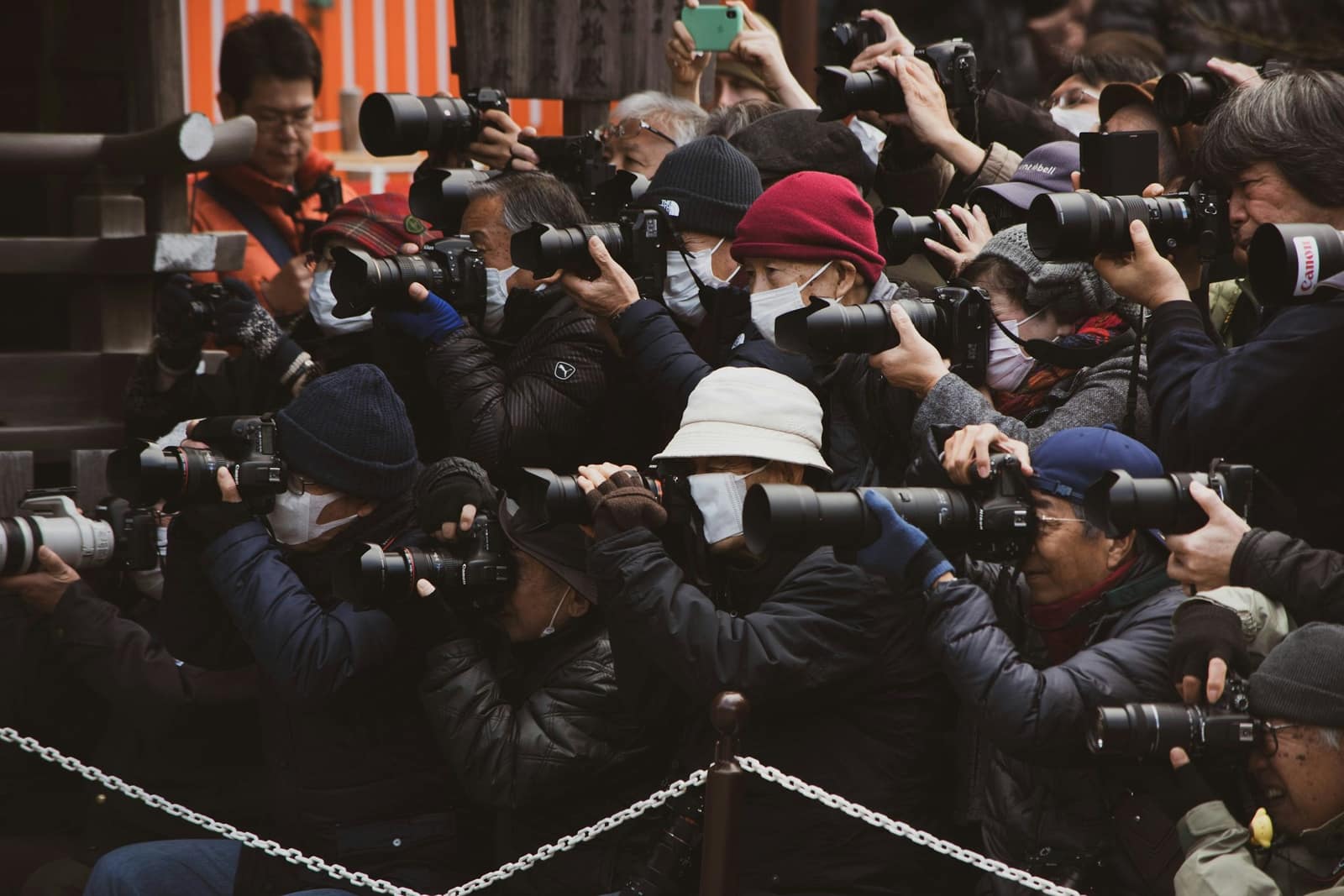 A crowd of photographers with long lenses pressed against a chain barrier